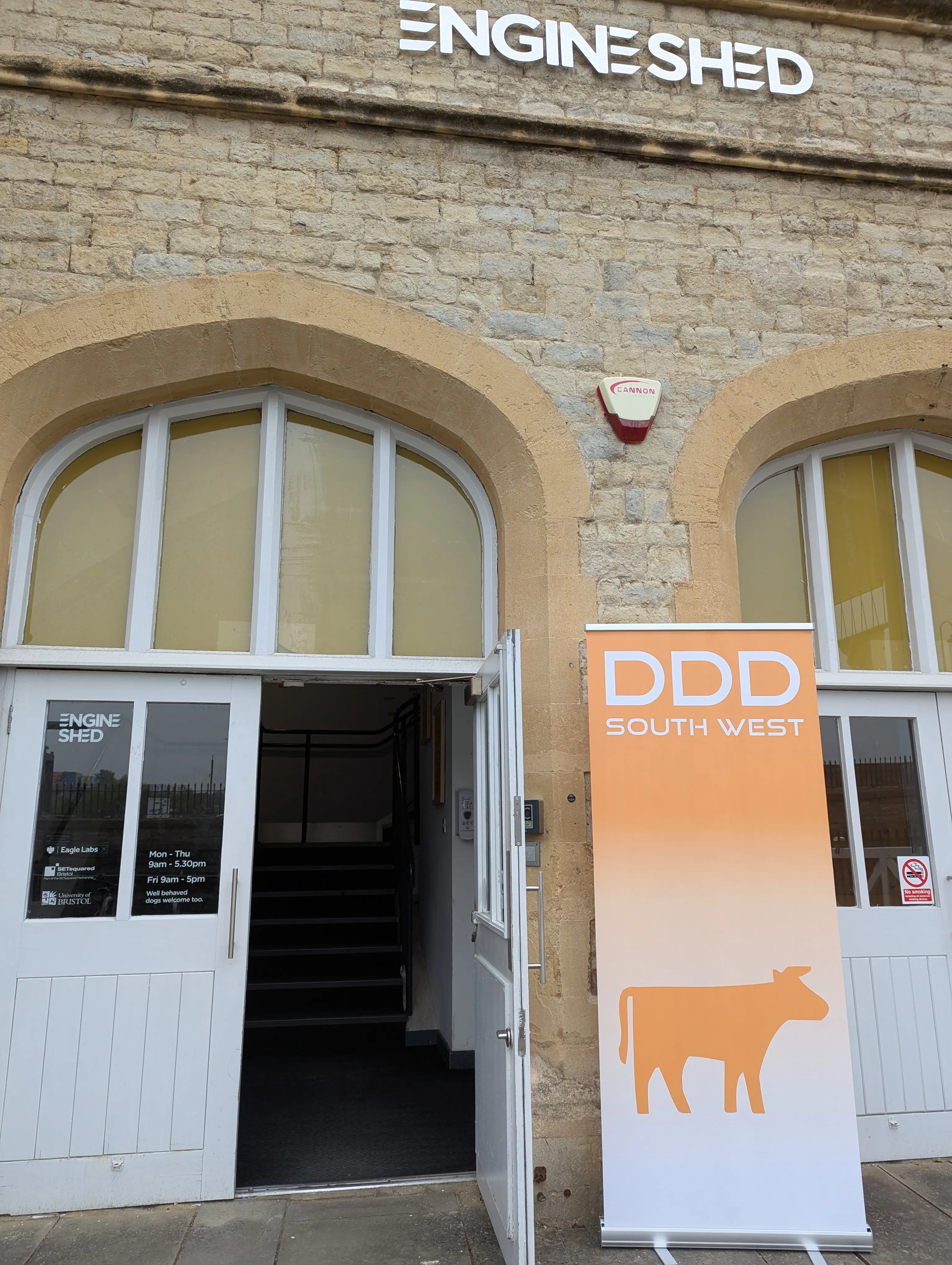 An image of the front door to the Engine Shed building, there is a popup sign by the side of the door that reads 'DDD South West' with an outline of a cow.'